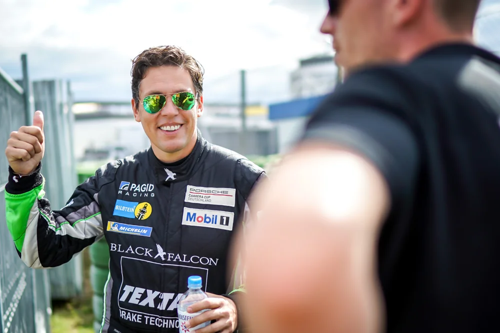Carlos Rivas smiling in racing overalls in the paddock
