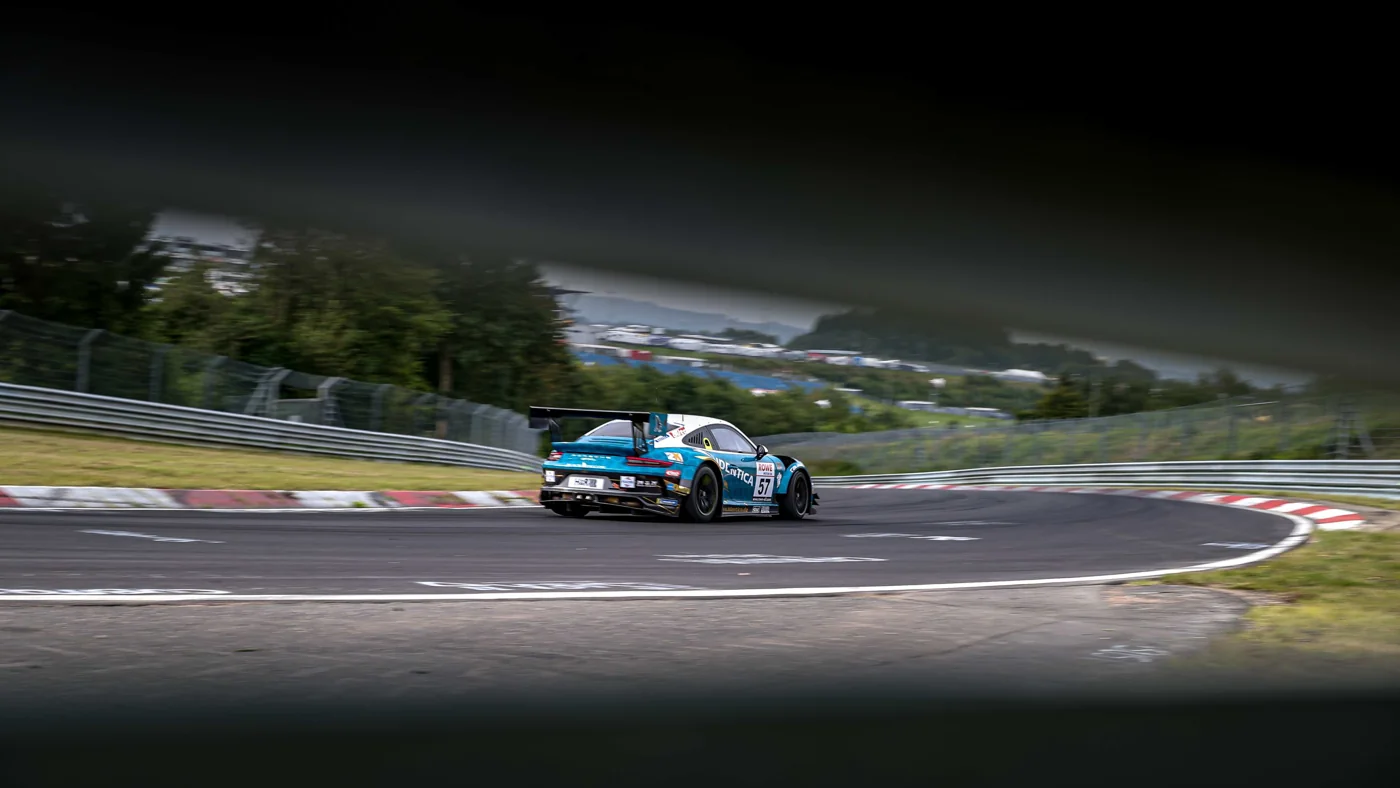 A Porsche on the Nürburgring, with hills and forest behind it